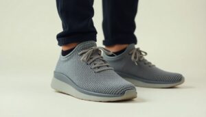 A person wearing dark pants and light grey Nexus Knit minimalist footwear by Xero Shoes with white soles, standing on a light surface. The shoes feature laces and a textured pattern, showcasing modern design.